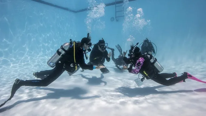 A dive instructor teaching two students underwater in calm, clear water
